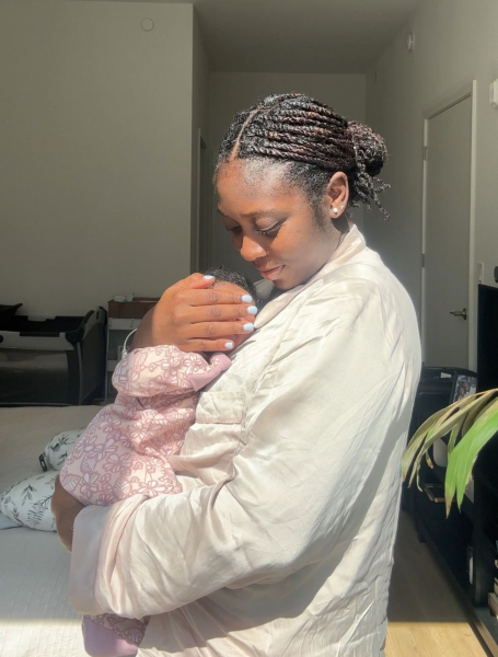 Black women holding baby in sunlight.